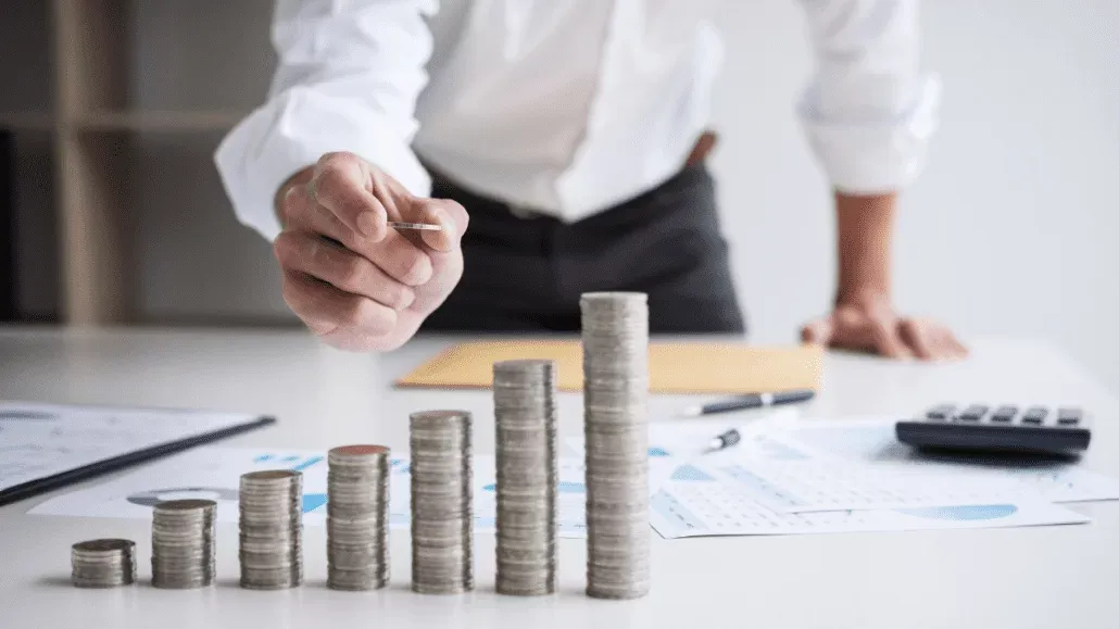 Seorang pebisnis menumpuk koin di atas meja dengan dokumen keuangan dan kalkulator